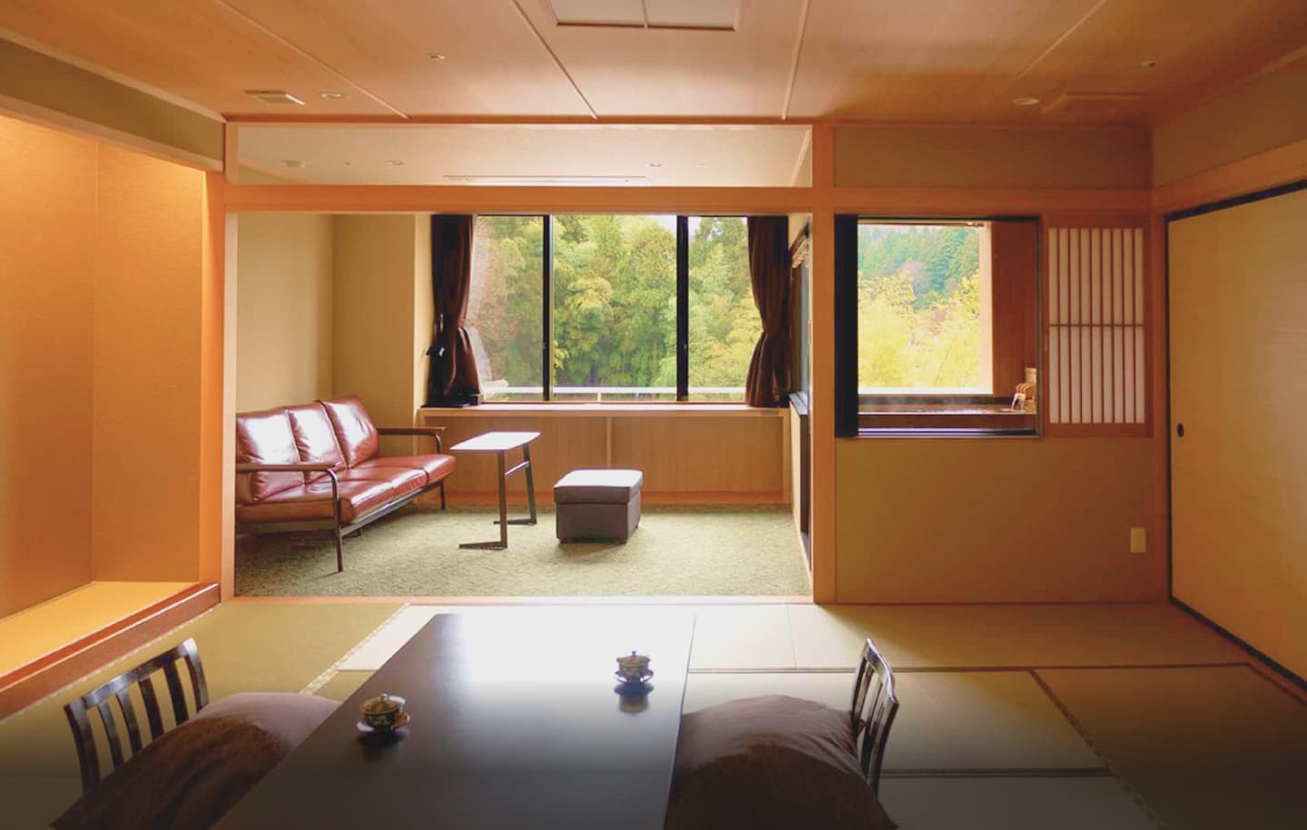 窓から見える紅葉と山々を望む、和室の客室。ソファとローテーブル、畳敷きの床に低めのテーブルが配置されている。