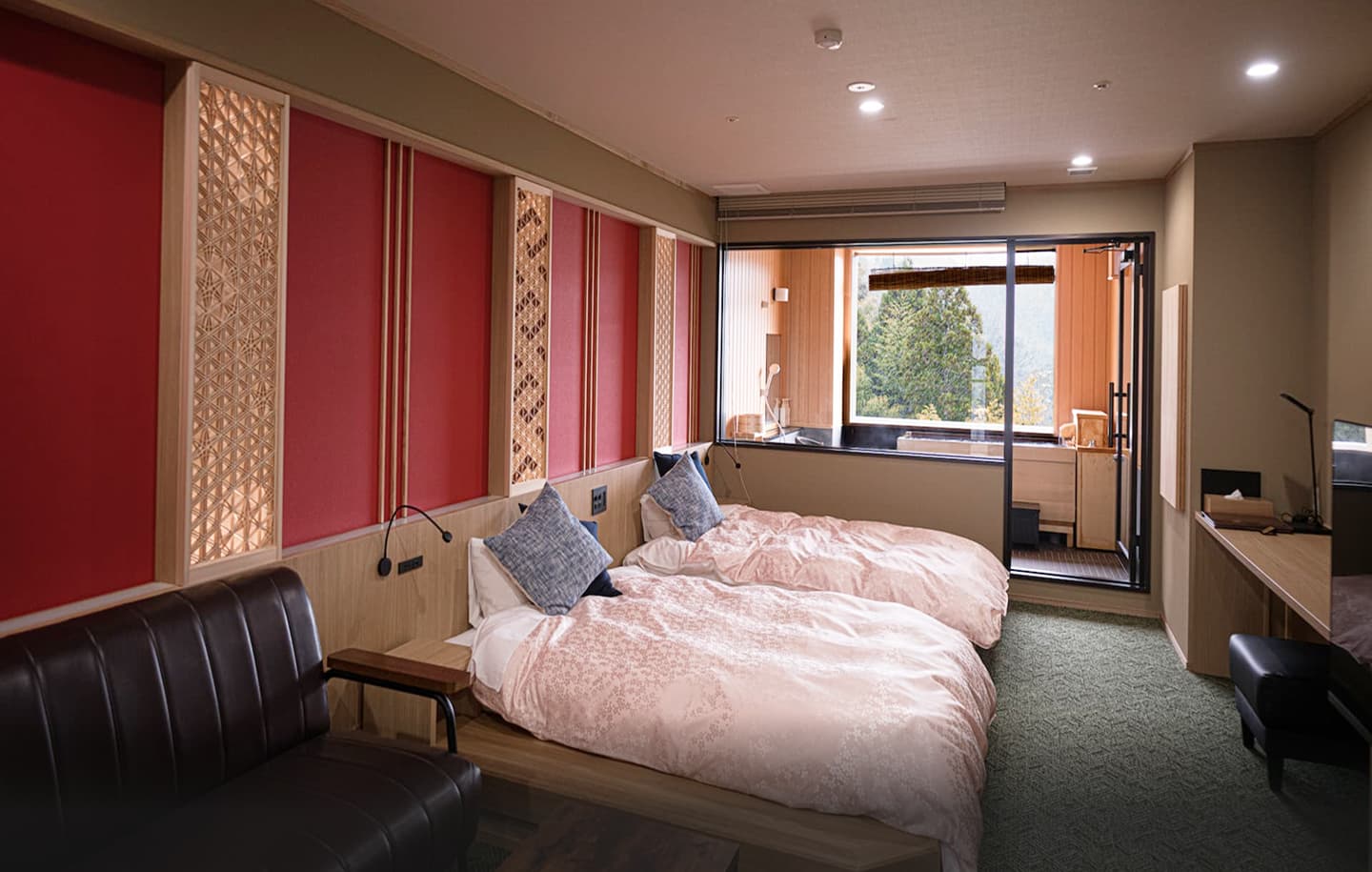 鮮やかな赤色のアクセントウォールが特徴的な、広々としたツインベッドルームの全景。手前にはゆったりとした革製のアームチェアとサイドテーブルが配置され、その奥には白い掛け布団のツインベッドが並んでいる。